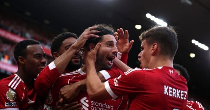 Soccer players in red uniforms celebrate a goal on the field, with one player being congratulated by his teammates as fans capture the moment for TikTok.