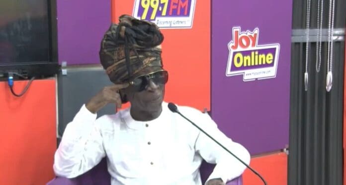 An older man wearing sunglasses and a traditional headwrap sits in a studio in front of Joy FM and MyJoyOnline signs, perhaps ready to discuss his new book or share memories of Kojo Antwi.
