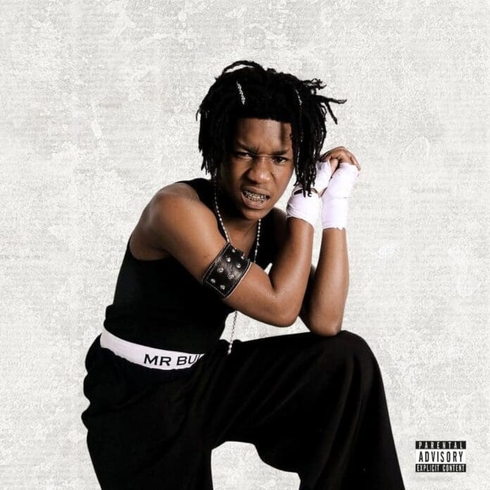 Young person with braided hair and braces poses in black clothing with white hand wraps against a plain background; "LaCabra" debut album parental advisory label is visible in the bottom right corner.