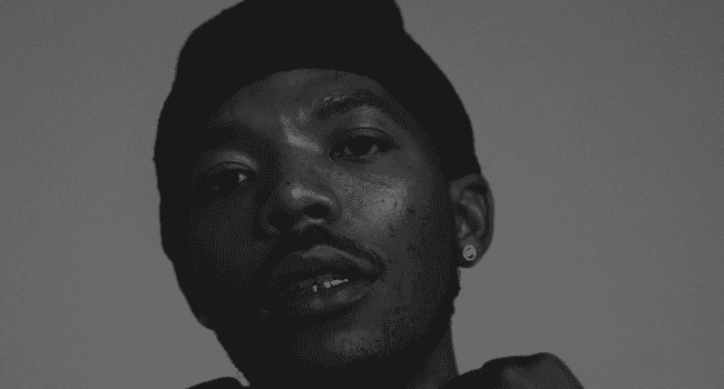 A person wearing a beanie and earring looks at the camera in a black and white portrait, capturing a vibe reminiscent of MashBeatz’s signature style.
