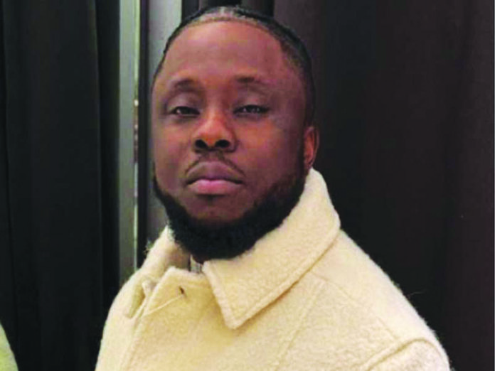 A man with short hair and a beard wears a light-colored, textured coat, standing in front of a dark background—a look reminiscent of Grammy winners captured on THISDAYLIVE.