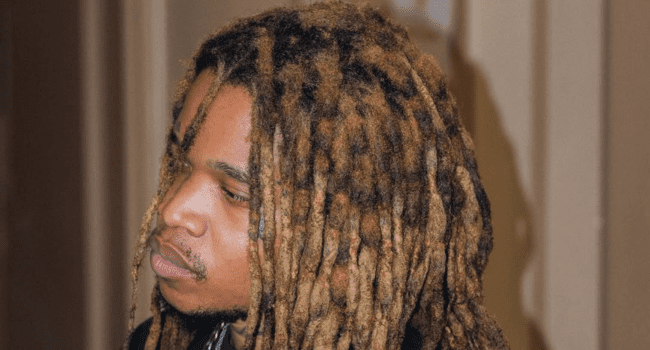 A person with long, thick, light brown and dark brown dreadlocks is looking slightly downward and to the side indoors, reflecting on personal transformation.
