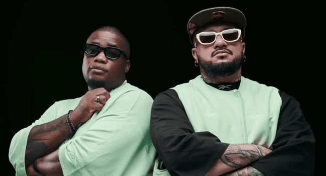 Two men wearing mint green shirts and sunglasses stand side by side against a black background, both facing forward with serious expressions—these could be the singing rappers of Shishiliza, exuding cool Venom energy with arms crossed or folded.