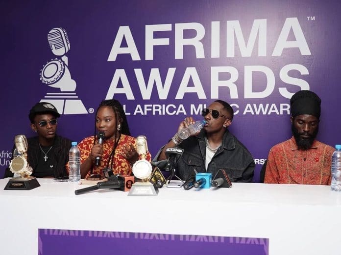 Tanzania-Press-696x522.jpeg Four people, including AFIRMA Winners like Folex and Juma Jux, sit at a press conference table with microphones and trophies, in front of an "AFRIMA Awards" banner.