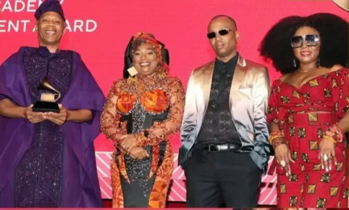 Four people dressed in colorful formal attire stand on stage, one holding a Lifetime Achievement Award, in front of a red backdrop—a fitting celebration for an event inspired by the legacy of Afrobeat and Fela Kuti.