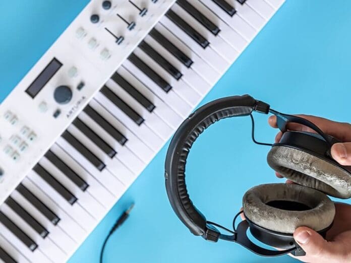 A person holds a pair of headphones near a white electronic keyboard on a blue surface, ready to create an electrifying sound.
