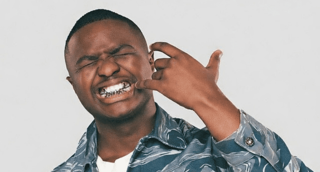 A person wearing a patterned shirt shows their silver grillz while making a hand gesture, eyes closed and facial expression suggesting excitement—channeling the energy of Spotify Streams and Girls & MP3’s.