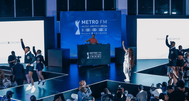 Performers dance and sing on stage at the Metro FM Music Awards 2026, with a DJ at a booth as the crowd cheers for nominees in the Best Hip Hop Category, capturing every moment on their phones.