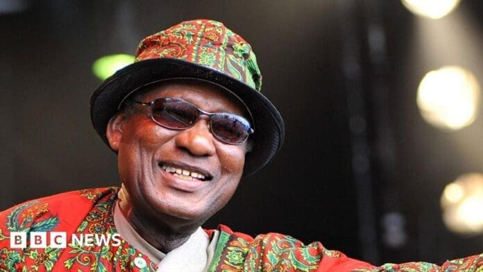 A smiling man wearing sunglasses, a patterned hat, and a matching outfit, with the BBC News logo in the bottom left corner—celebrating Ebo Taylor and Ghanaian highlife music.