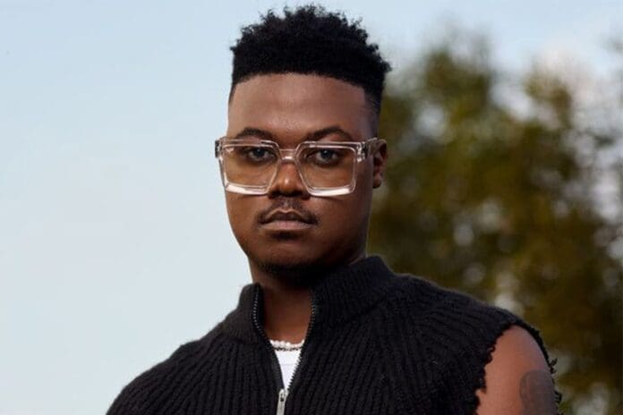 A person with short curly hair, clear glasses, and a sleeveless black top stands outdoors in front of blurred trees, ready to enjoy the Espinho Valentine’s Event.