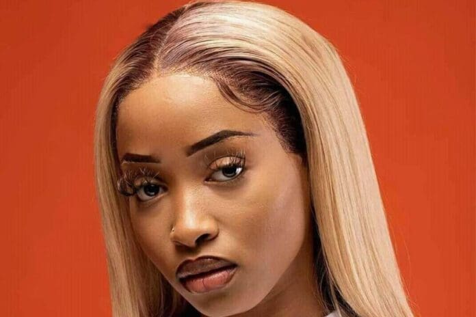 A woman with long, straight blonde hair and arched eyebrows looks at the camera against an orange background, channeling bold style reminiscent of performers at Afro Nation Portugal.