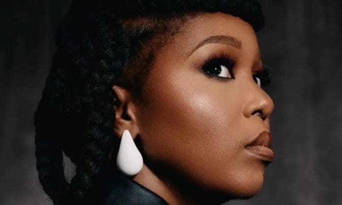A woman with braided hair, wearing white geometric earrings, looks over her shoulder against a dark background, evoking the vibrant energy of a live concert in Joburg.