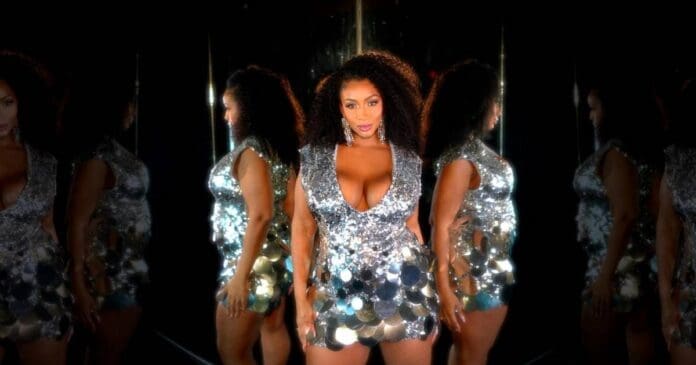 Nzinga Imani stands confidently in a silver, reflective sequin dress against a dark background, her reflections shimmering on both sides—radiating the same bold energy as her Afrobeats debut, "Drown.