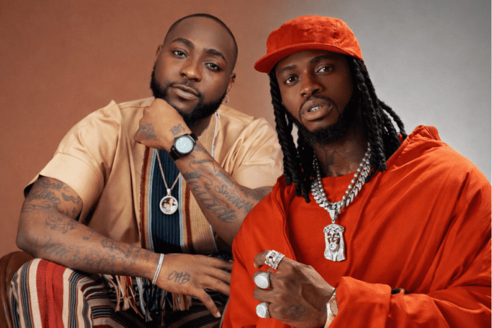 Two men posing together; one wears a tan shirt with striped pants and the other sports an orange outfit with a matching cap. Both display diamond jewelry and visible tattoos, capturing the stylish spirit of African music stars like Davido.