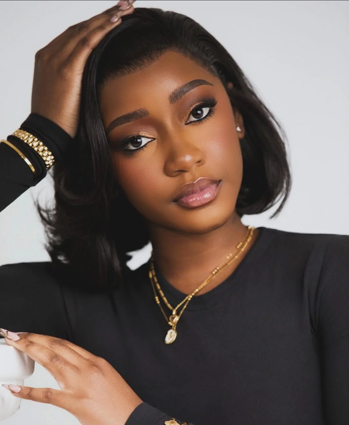 Ms. Gideon, a woman with short, styled black hair, wears a black top and gold jewelry as she poses with one hand on her head against a plain background—capturing the striking style seen in Sony Music Africa’s rising stars from Namibia.