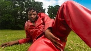 Person in a red outfit lies on green grass outdoors with trees and blue sky in the background, embracing an Afro-pop vibe that feels just like an Obacino "Like To Party" moment.
