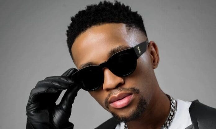 A man wearing black sunglasses, a black glove, and a chain necklace looks at the camera against a plain background, capturing the bold style often seen in amapiano songs and Music In Africa in 2026.