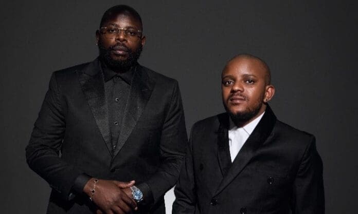 Two men wearing black suits and white shirts pose against a plain dark background, channeling the iconic style of Scorpion Kings, renowned amapiano artists on Spotify.