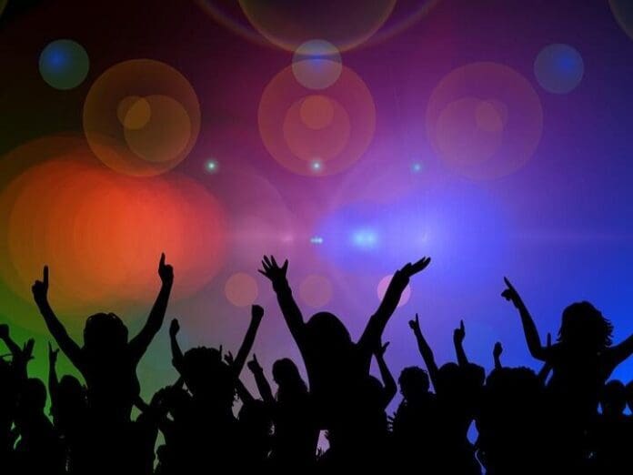 Silhouettes of people dancing with their hands raised against a colorful, abstract background with various light effects, reminiscent of an America steeped in the rhythms of blues music.