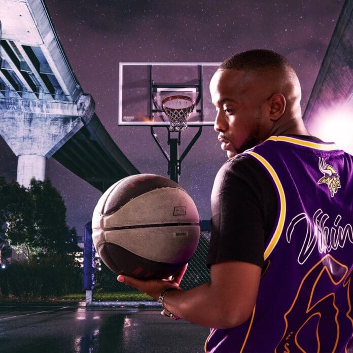 A man in a purple basketball jersey holds a basketball on an outdoor court at night, with a bridge and basketball hoop in the background, as Shaunmusiq plays softly in the distance.