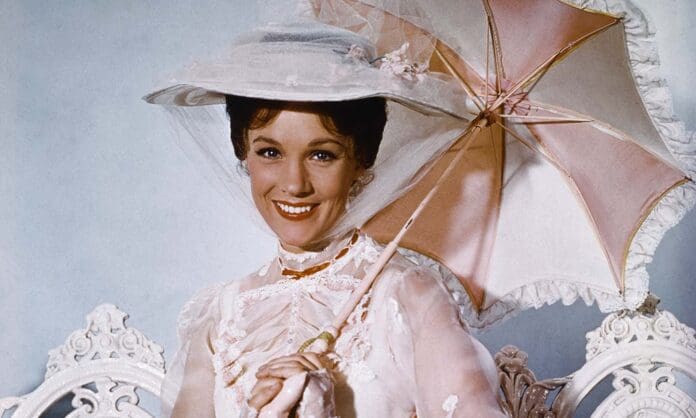 A person dressed in vintage clothing, holding a parasol and wearing a hat, smiles at the camera, reminiscent of Disney's Heroes in uDiscover Music's defining songs collection.