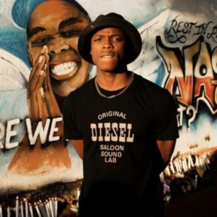 A person wearing a 'Diesel' T-shirt and a hat stands in front of a mural featuring a smiling person and the text 