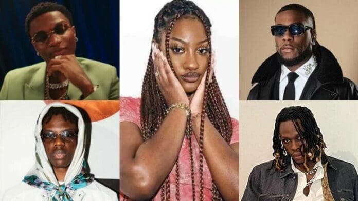 A collage of five individuals at the iHeartRadio Music Awards; one on the left wearing a green suit and glasses, a woman in the center with braided hair, and three men on the right wearing stylish outfits and accessories. Among them, Wizkid and Burna Boy stand out with their signature flair.