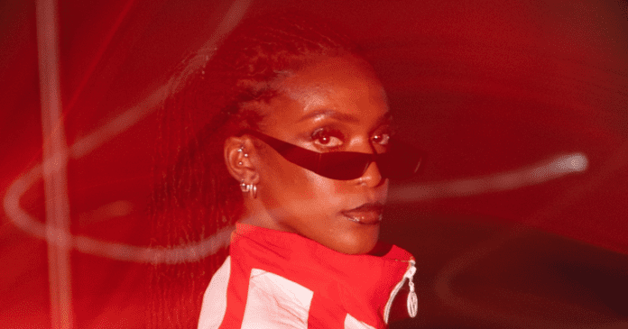 A person with dark braided hair, wearing sunglasses and a red and white jacket reminiscent of DEJA's style, is looking over their shoulder towards the camera. The image has a red overlay effect that gives it an Afrobeats vibe.