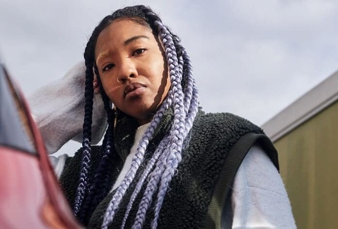 A woman with braided hair standing next to a car at the PAM Club.