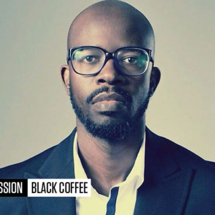 A man wearing glasses and a suit enjoys black coffee.