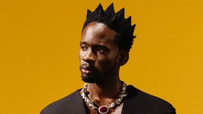 A man in a black shirt with a crown on his head, Mr. Eazi displays his Pan-African pride and global purpose on 'The Evil Genius' - Rolling Stone.