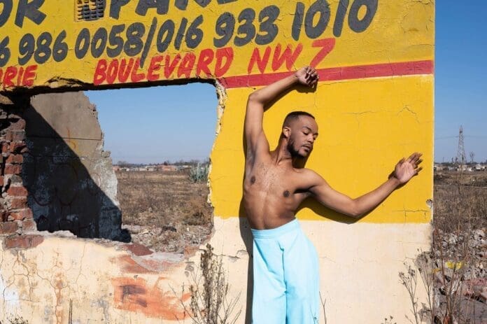 A man posing in front of a building, capturing South Africa's vibrant youth culture through photography.