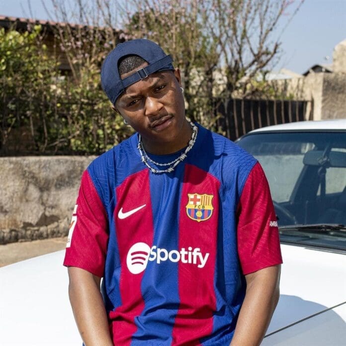 A man in a Barcelona jersey sitting on a car.