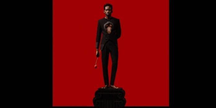 A man holding a gun in front of a red background featuring Mr Eazi.