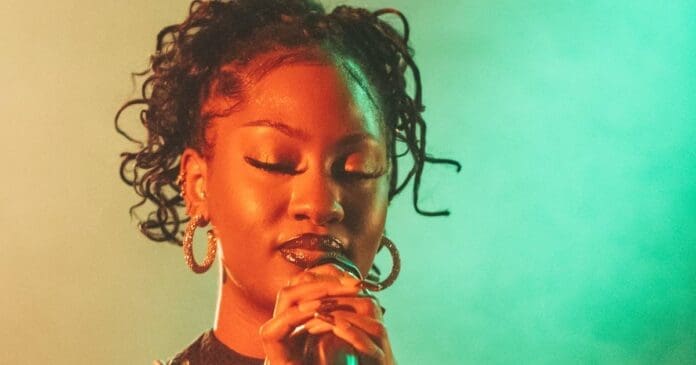 A woman with dreadlocks singing into a microphone at the Soul Train Awards 2023.