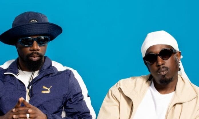 Two men wearing hats and sunglasses on a blue background in Team Salut's Wow single featured in iPhone 15 commercial.