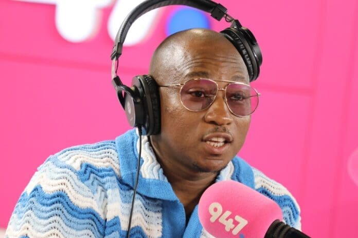 A black man wearing headphones in front of a pink background, Khuli Chana speaking his life into existence.