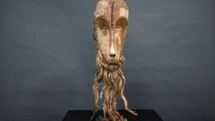 An African wooden mask with long hair on a stand.