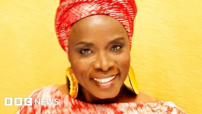 Angélique Kidjo, wearing a red turban, smiling at the camera with Africa's tsunami of talent.