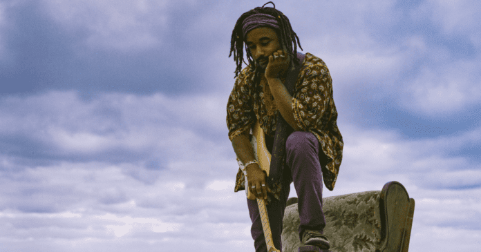 Owusu, a Best Musician nominee at the Music Victoria Awards, is seen sitting on top of a rock with his distinctive dreadlocks.