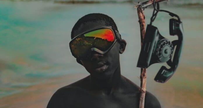 A black man with goggles holding a stick on the beach in October 2023.