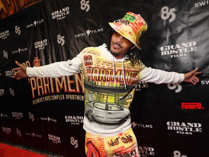 A man standing on a red carpet with a hat on his head, enjoying the vibes of an amapiano train.