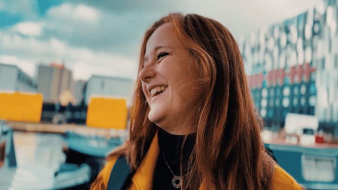 A young woman is smiling in front of a building at LBBOnline.