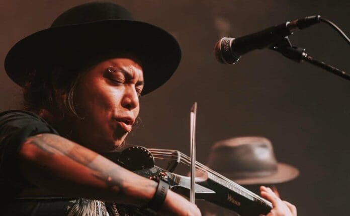 An Indigenous artist, wearing a black hat, playing a violin.