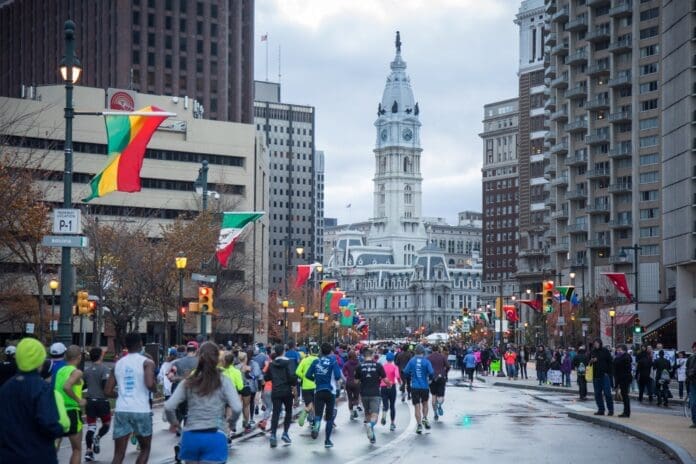 A group of people participating in the Philadelphia Marathon Weekend running down a city street.