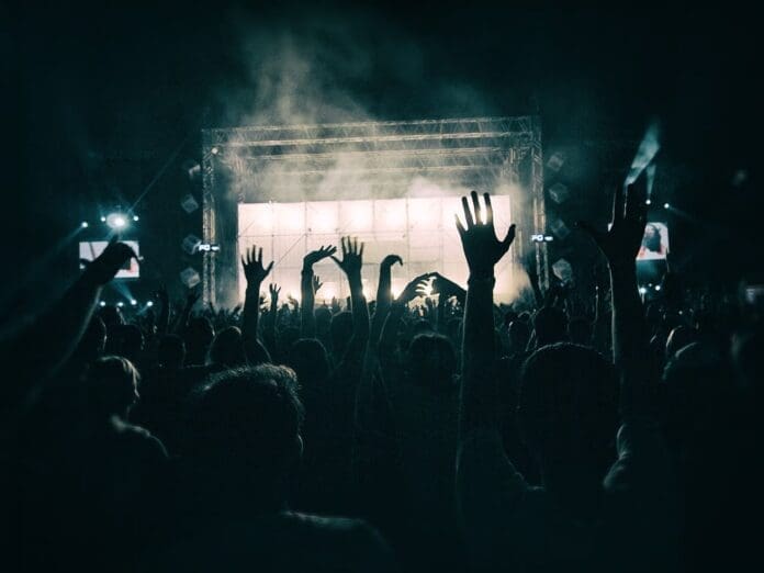 A lively crowd at a concert, enthusiastically raising their hands in sync with the music.