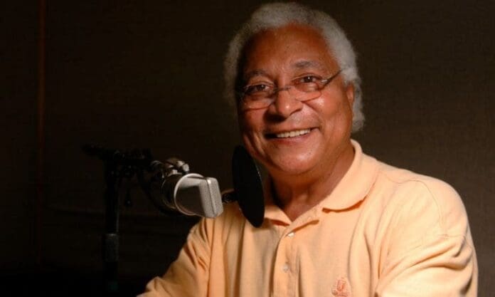 An older man smiling in front of a microphone, celebrating the 35th anniversary of Afropop Worldwide.