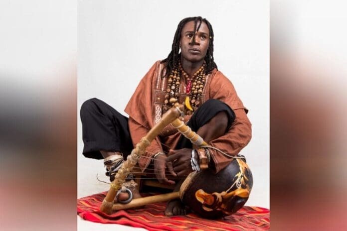 An artist with dreadlocks sitting on a rug with a drum, utilizing music therapy.