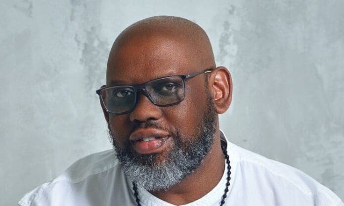 At the African Music Summit in London, a stylish black man with glasses and a beard strikes a pose for a photo.